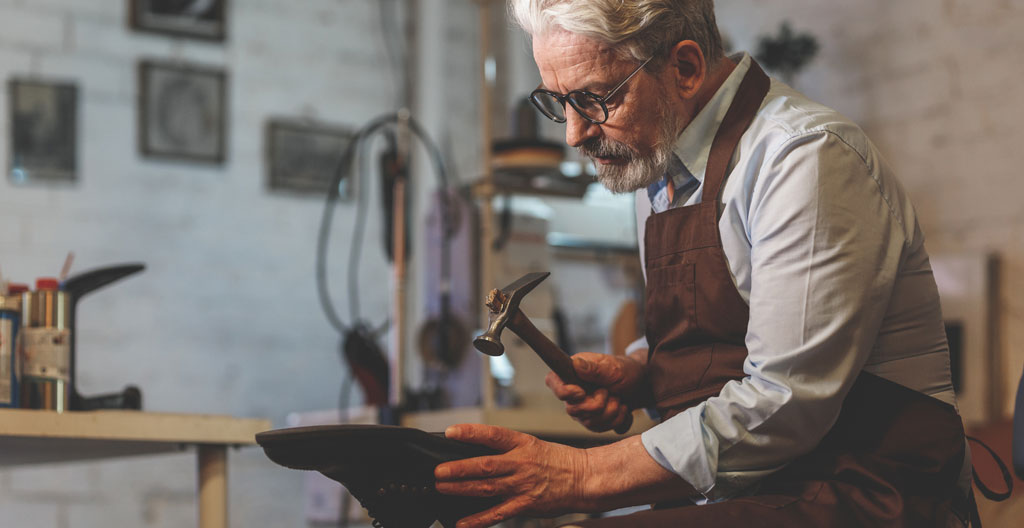 Mains d'un artisan travaillant sur une chaussure dans un atelier, avec des outils de cordonnerie visibles autour