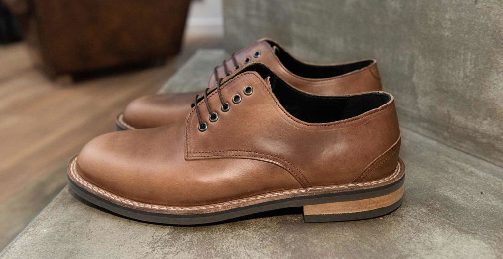Vue de profil d'une chaussure posée sur une surface en bois, montrant les coutures latérales et la semelle